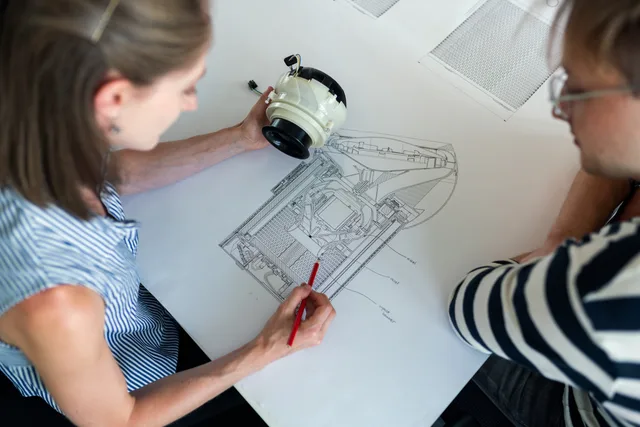 Two engineers collaborate over a detailed technical design blueprint, focusing on innovation and planning. Branchen-Zulieferer in Österreich finden: Wege und Kriterien